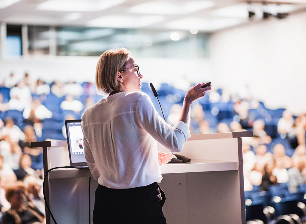 Referentin am Pult nutzt intuitive Präsentations- und Steuerungstechnik im Auditorium.