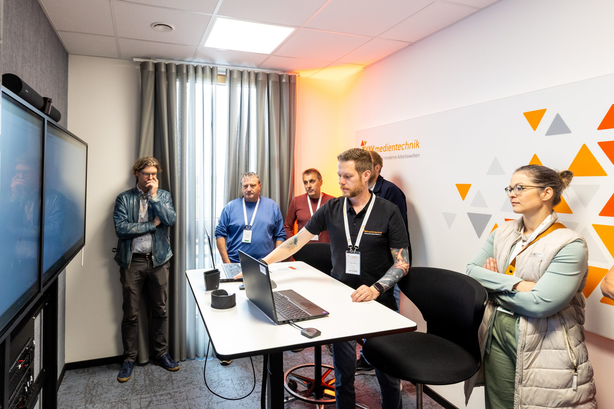 Besucher verfolgen eine Technik-Demo im Videokonferenzraum mit Dual-Display und Laptop