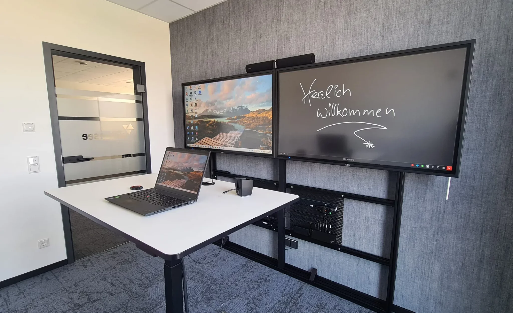 Touch-Display mit Begrüßungstext „Herzlich willkommen“ und aktivem Desktop auf zweitem Bildschirm