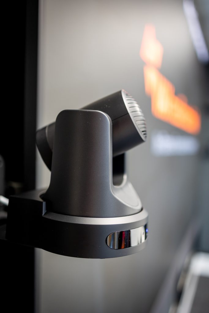 Intelligente Raumkamera im Showroom Igling Wandmontierte PTZ-Kamera im Raum Isar mit unscharfem VAVmedientechnik-Logo im Hintergrund