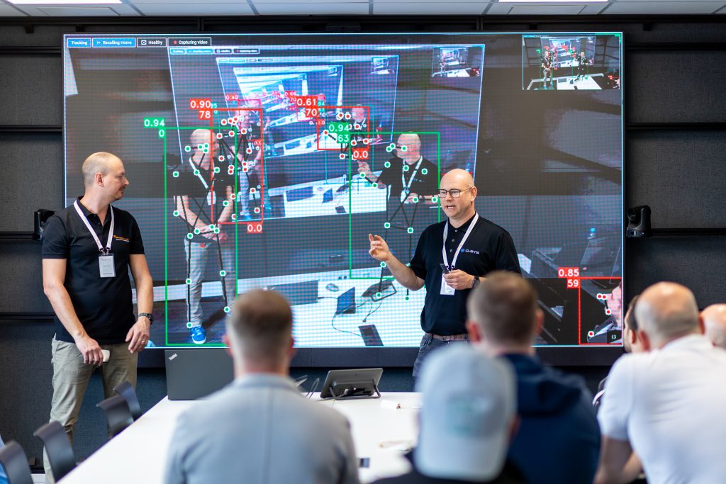 Teilnehmer verfolgen Präsentation mit Smart‑Panels im Hintergrund