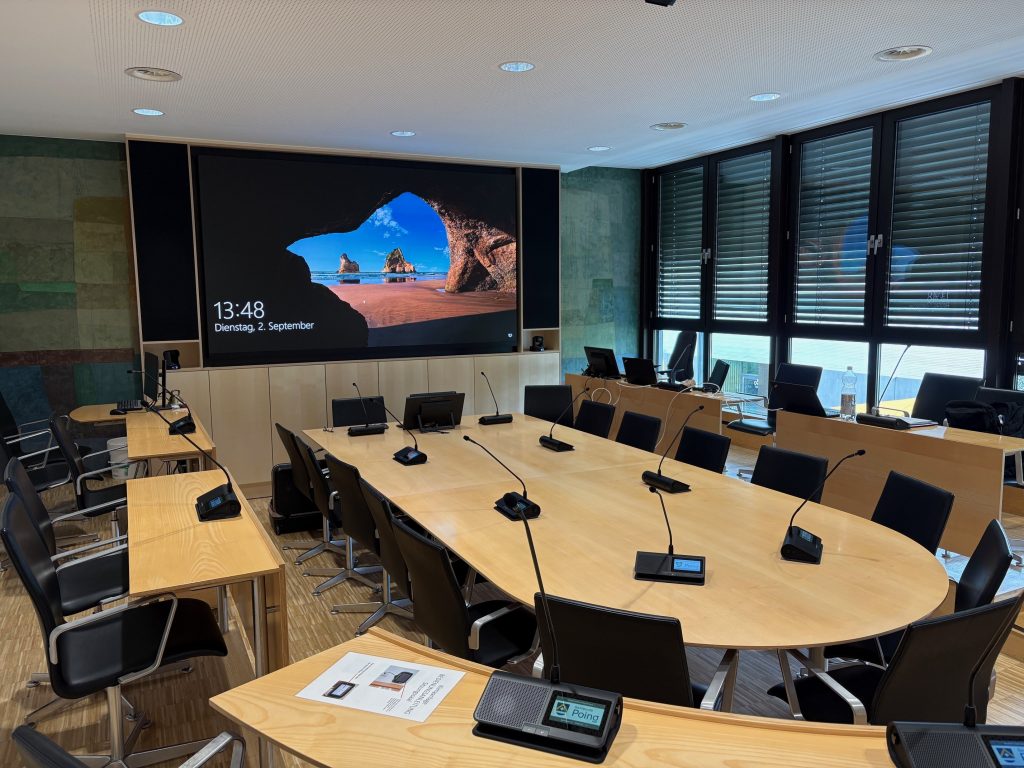 Blick auf Konferenztisch mit drahtlosen Sprechstellen und LED-Wand